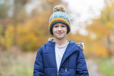 Boy wearing knit hat staring while standing in forest - WPEF04075