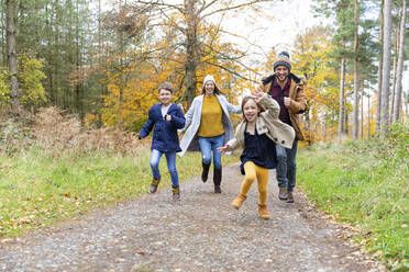 Glückliche Familie beim gemeinsamen Laufen auf einem Waldweg - WPEF04082