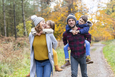 Eltern nehmen ihre Kinder beim Herbstspaziergang im Wald huckepack - WPEF04085