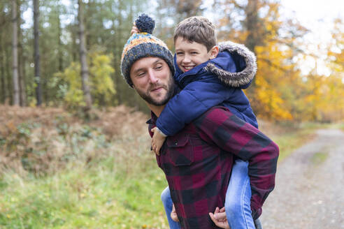 Lächelnder Junge genießt es, im Wald huckepack auf seinem Vater zu sitzen - WPEF04090