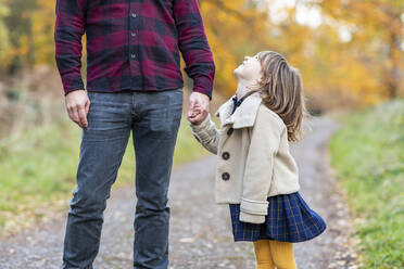 Lächelnde Tochter, die die Hand des Vaters hält, während sie am Waldweg steht - WPEF04095