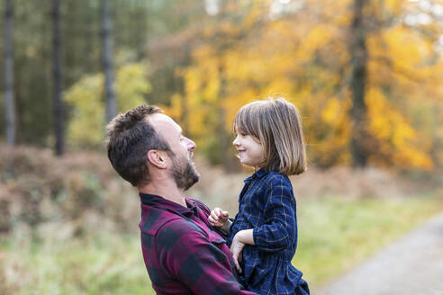 Vater trägt seine Tochter in den Armen, während er im Wald steht - WPEF04098