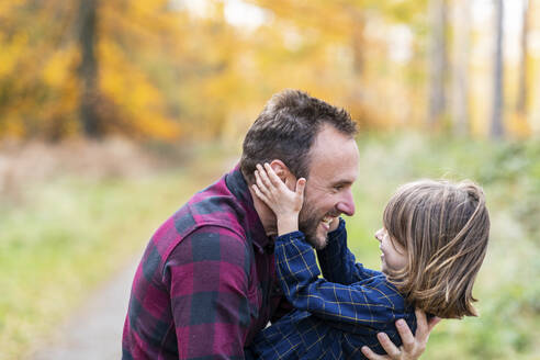 Lächelnder Vater trägt seine Tochter beim Spielen im Wald - WPEF04099