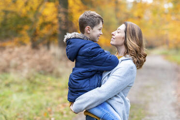 Mutter trägt lächelnden Sohn in den Armen, während sie im Wald steht - WPEF04105