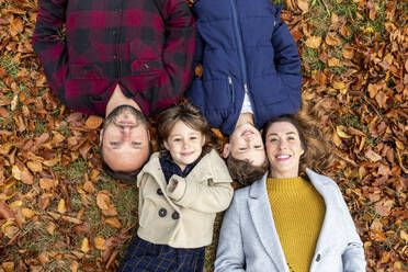 Lächelnde Familie auf einem gefallenen Blatt im Wald im Herbst liegend - WPEF04123