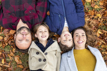 Familie lächelnd beim Ausruhen auf einem gefallenen Blatt im Wald im Herbst - WPEF04124