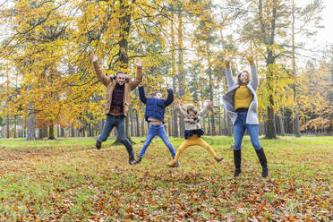 Playful family with hand raised jumping together in forest - WPEF04125