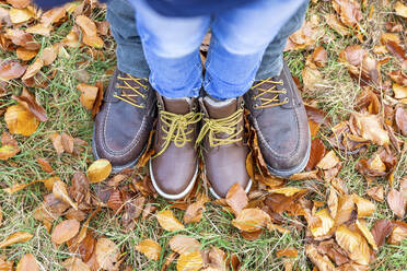 Father and son wearing leather shoe standing together on fallen leaf - WPEF04126