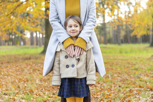 Lächelnde Tochter schaut weg, während sie mit ihrer Mutter im Wald steht - WPEF04129