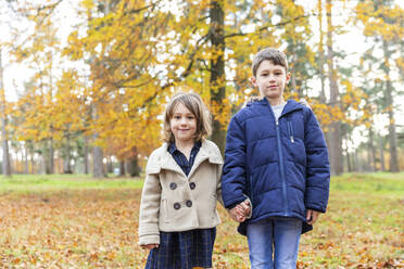 Cute sister holding brother hand while standing at forest - WPEF04136