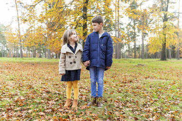 Sibling looking at each other while standing in forest during autumn - WPEF04137