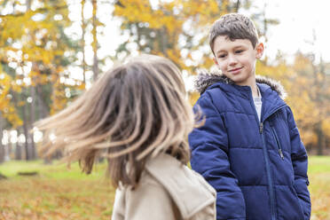 Bruder sieht seine spielende Schwester an, während er im Wald steht - WPEF04139