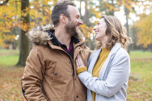 Couple smiling while looking at each other standing in forest - WPEF04144