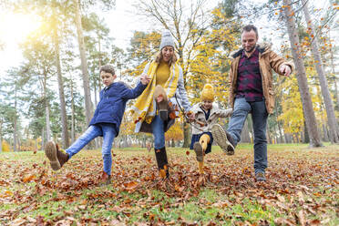 Family holding hands while kicking fallen leaf at forest - WPEF04158