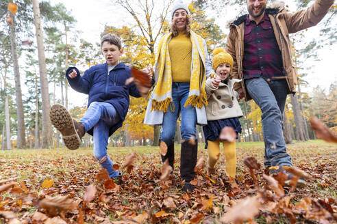 Lächelnde Familie spielt mit gefallenen Blättern beim Spaziergang im Wald - WPEF04159