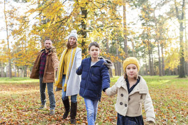 Familie hält sich gegenseitig an den Händen beim Spaziergang im Wald - WPEF04164