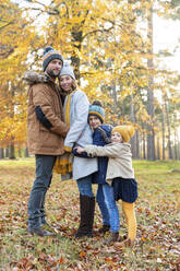 Family embracing each other while standing in forest during autumn - WPEF04167