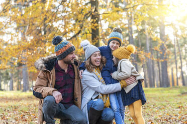 Mother embracing children while crouching by man in forest - WPEF04168