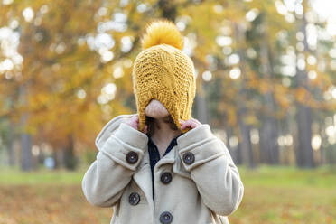 Girl pulling knit hat while playing in forest - WPEF04175