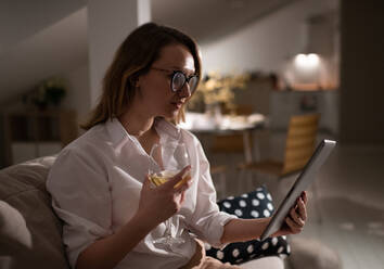 Junge Frau mit einem Glas Wein und einem Tablet zu Hause - CAVF93342