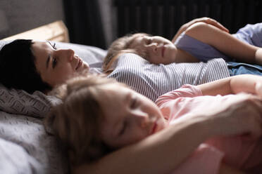 Mother hugging sleeping daughters in morning at home - CAVF93352