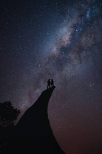 Couple standing on the edge of a cliff during the night sky - CAVF93431