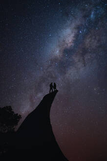 Couple standing on the edge of a cliff during the night sky - CAVF93431