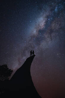 Paar, das am Rande einer Klippe steht und den Nachthimmel betrachtet - CAVF93431