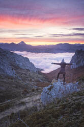 Woman waving at sunrise over sea of clouds - CAVF93439