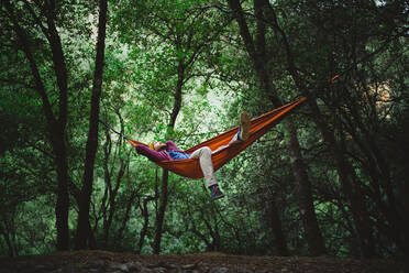 Young male rests on a hammock in the middle of the forest - CAVF93442