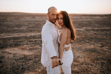 Side view of peaceful couple in white outfit standing together in savanna and looking at camera - ADSF20759