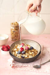 Hand with a jug pouring milk to granola with berries - ADSF20765