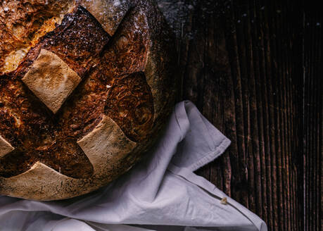 Draufsicht auf leckeres Brot mit Kruste auf Serviette auf Holztisch in Bäckerei platziert - ADSF20768