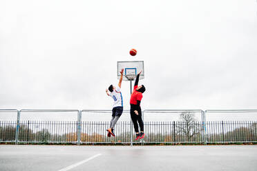 Junge männliche Freunde spielen Basketball auf dem Platz und springen durch den Reifen. - ADSF20770