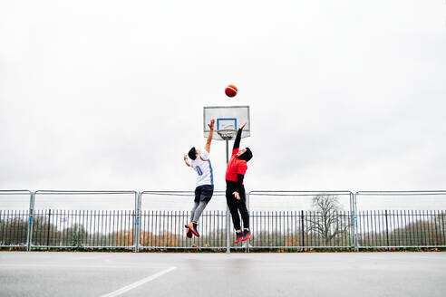 Junge männliche Freunde spielen Basketball auf dem Platz und springen durch den Reifen. - ADSF20770