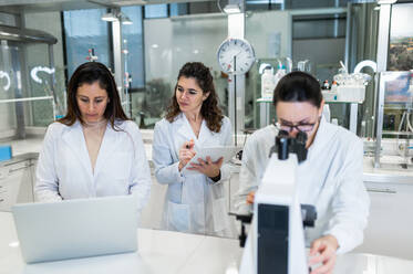 Gruppe professioneller Wissenschaftlerinnen mit Mikroskop und Laptop bei der gemeinsamen Forschung in einem modernen Labor - ADSF20793