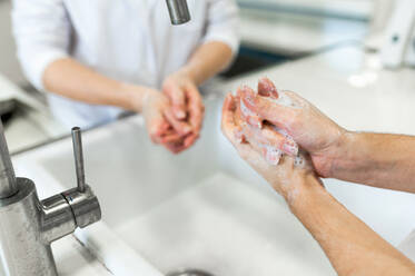 From above of female scientists in white coats and protective masks washing hands before conducting chemical experiment in modern laboratory - ADSF20796