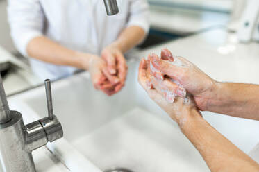 Von oben: Wissenschaftlerinnen in weißen Kitteln und mit Schutzmasken waschen sich die Hände, bevor sie in einem modernen Labor ein chemisches Experiment durchführen - ADSF20796