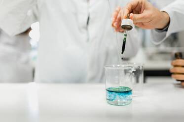 Professionelle Wissenschaftlerin im weißen Kittel und mit Schutzmaske führt ein chemisches Experiment mit einer blauen Flüssigkeit in einem modernen Labor durch - ADSF20799