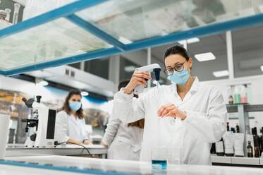 Professionelle Wissenschaftlerin im weißen Kittel und mit Schutzmaske führt ein chemisches Experiment mit einer blauen Flüssigkeit in einem modernen Labor durch - ADSF20800