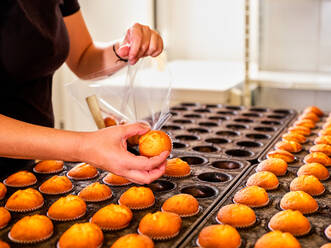 Anonymer Bäcker verpackt frisch gebackene und abgekühlte Muffins in eine Plastiktüte, während er in einer professionellen Bäckerei arbeitet - ADSF20812