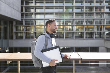 Smiling mature male professional holding files while standing against building - JPTF00669