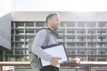 Älterer Geschäftsmann mit Rucksack, der an einem Gebäude steht und wegschaut - JPTF00672