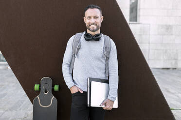 Smiling male entrepreneur with hand in pocket standing against wall - JPTF00675