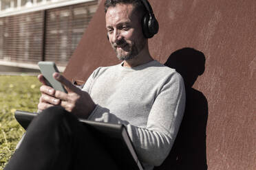 Mature man listening music through headphones while using smart phone - JPTF00676