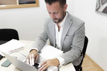Reifer Geschäftsmann mit Laptop bei der Arbeit im Büro - JPTF00677
