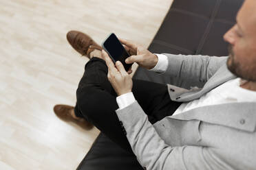 Male professional using smart phone while sitting on sofa in office - JPTF00682