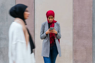 Arab female in hijab standing sending message on mobile phone and communication on social media standing on the street - ADSF20817