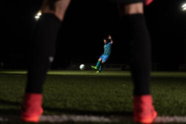 Anonymer Torwart, der das Tor schützt, während ein gegnerischer Spieler den Ball während eines Spiels auf dem Spielfeld tritt - ADSF20861