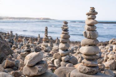 Malerische Szenerie von Zen-Steinpyramiden am Strand in der Nähe von wogendem Meer an einem sonnigen Tag in Vila Nova de Milfontes, Portugal - ADSF20864